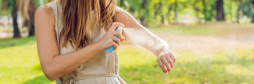 A woman using bug spray to keep mosquitos away.