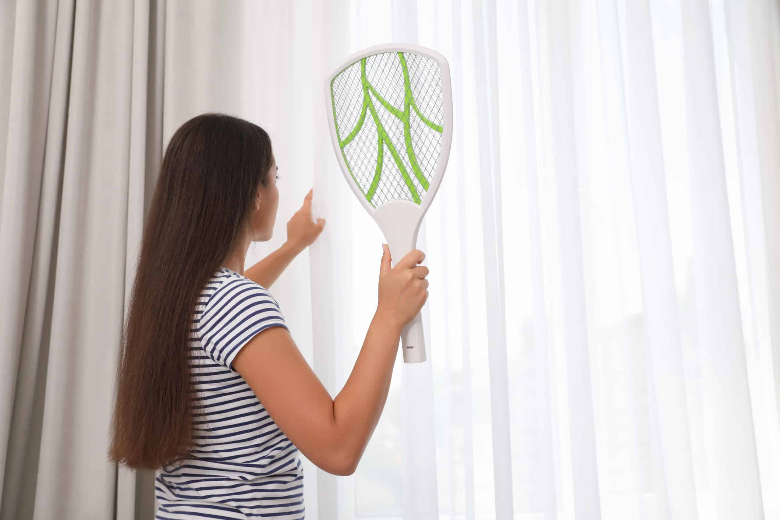 Young woman with electric fly swatter indoors, back view - Flying Insects killer