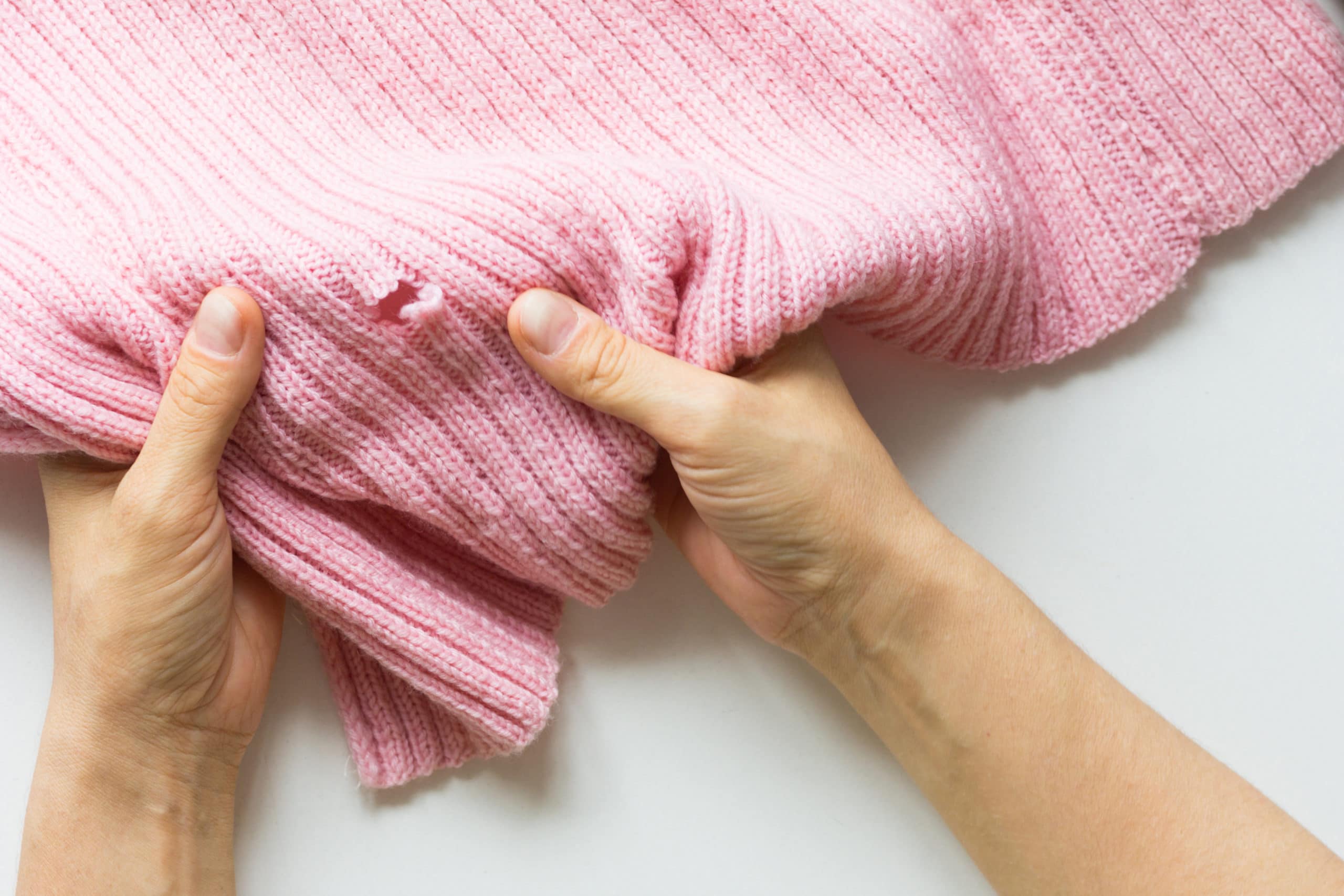 Woman hands holding the knitted thing with hole made by a clothes moth
