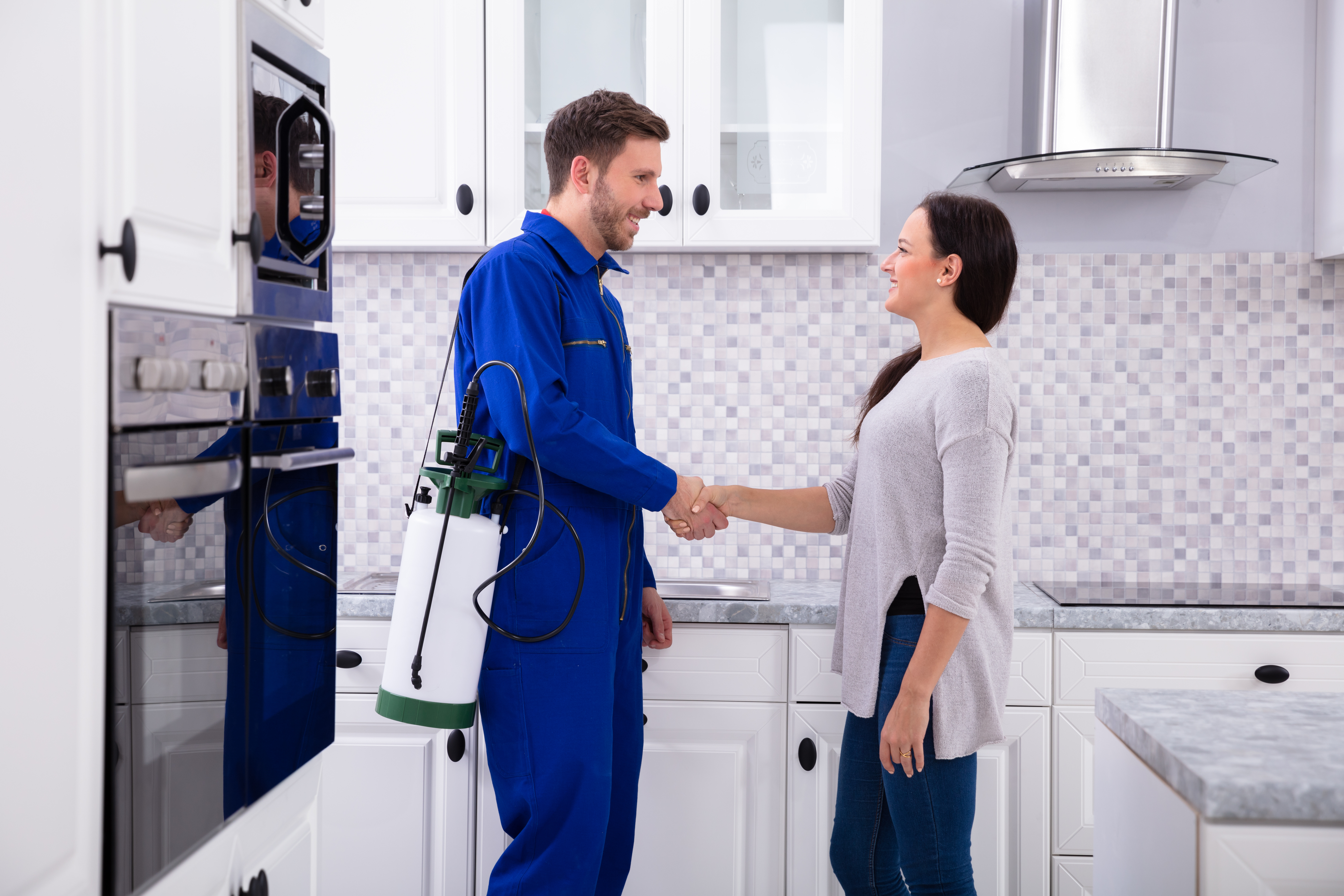 Male Pest Control Worker Shaking Hands With Happy Woman In Kitchen
