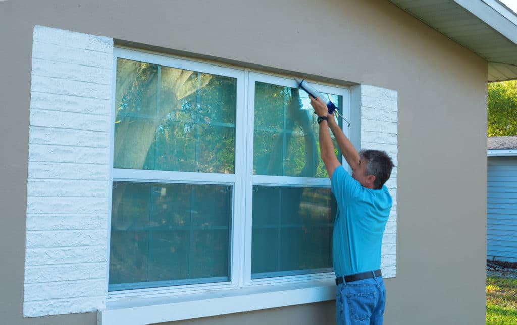A man caulking the exterior of his home to prevent an earwig infestation