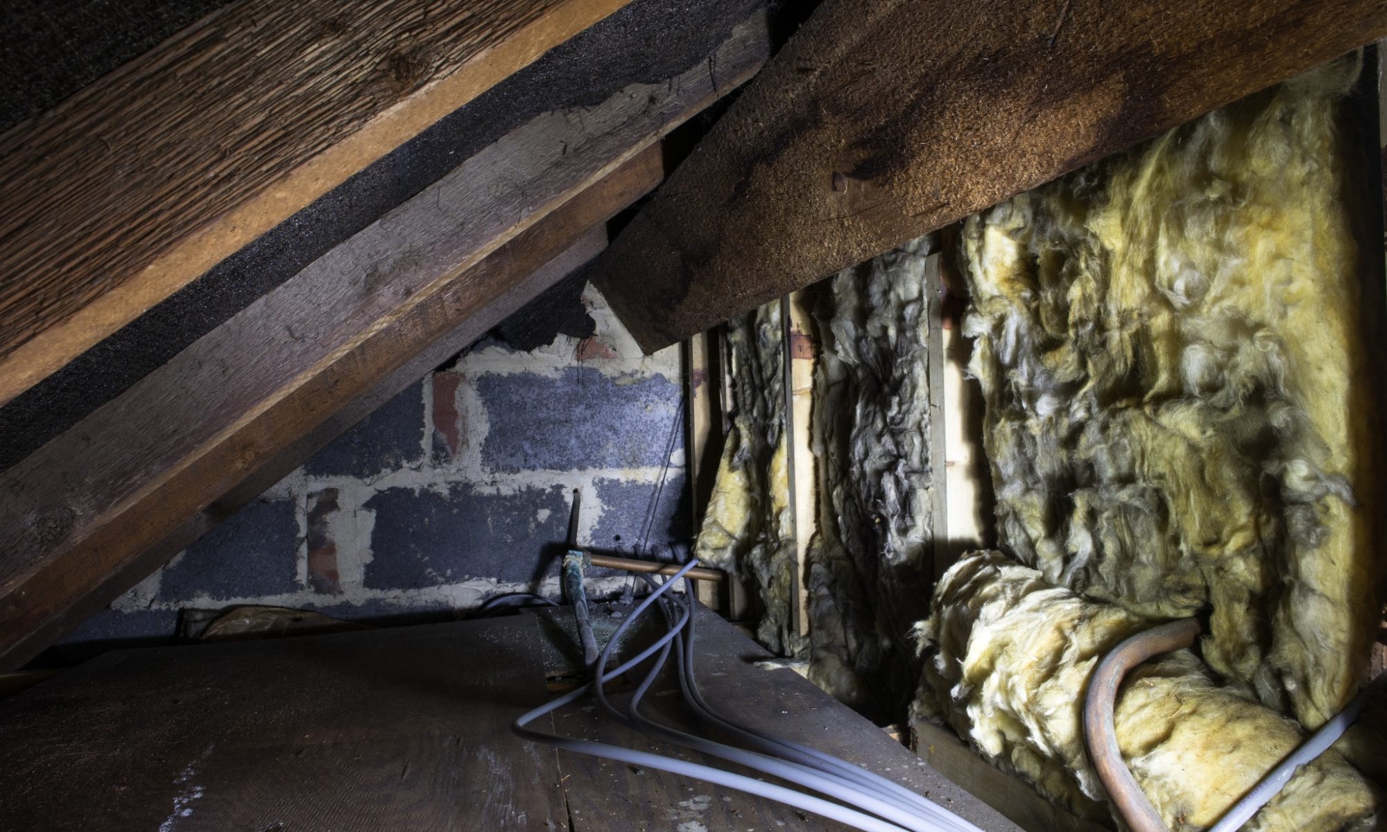 A crawl space with wooden beams and yellow insulation.