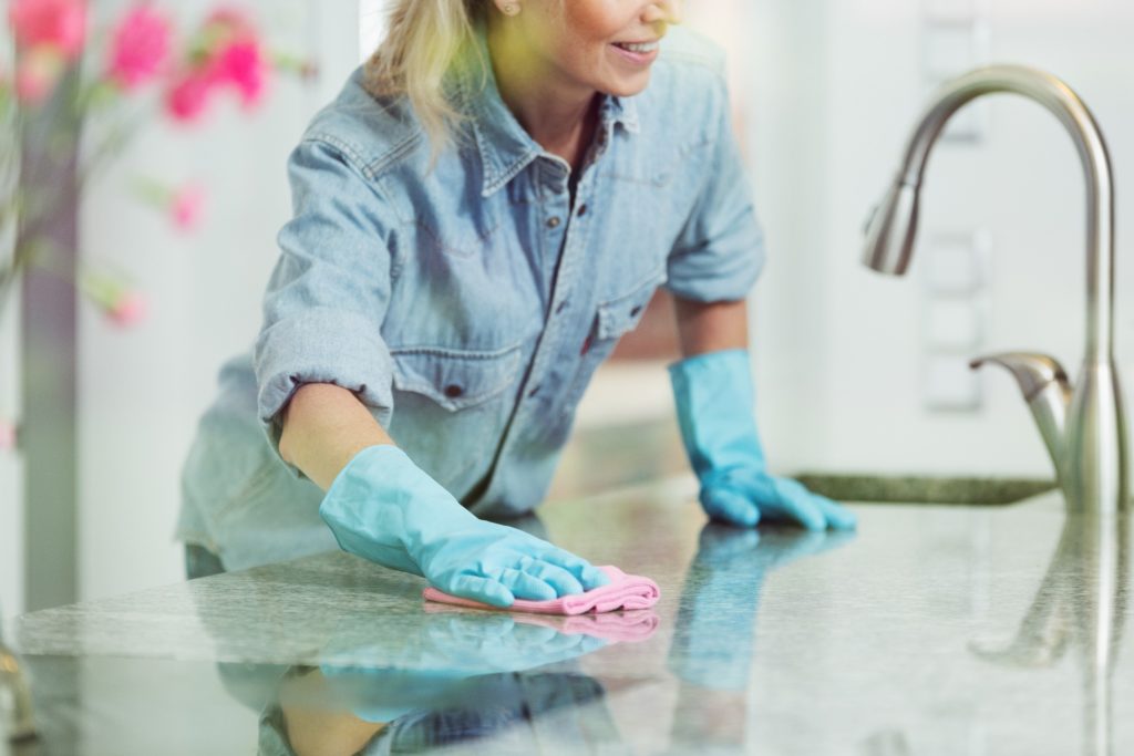 A woman wearing a denim shirt and blue rubber gloves wiping down her counter and spring cleaning to help prevent ants.